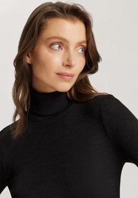 Schwarzer gerippter Rollkragenpullover mit tailliertem Design, strukturiertem Stoff und hohem Ausschnitt, ausgestattet mit langen Ärmeln und einer glatten Oberfläche.