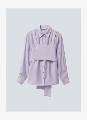 Λιλά πουκάμισο με μακρύ μανίκι και κουμπιά, με προσαρτημένο καβάλο cropped τοπ ως επικάλυψη και επιπλέον ύφασμα που κρέμεται κάτω από το τελείωμα του πουκαμίσου.