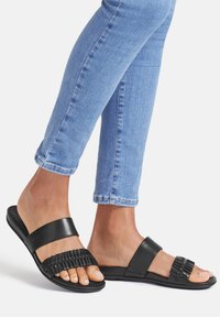 Svarta lädersandaler med en vävd remdesign, platt sula och minimalistiska detaljer, tillsammans med ljusblå tajta jeans.