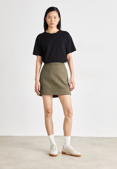 Svart bomull t-skjorte med korte ermer. Olivengrønn skjørt i skaterstil med elastisk midje. Hvite sokker og beige joggesko med gummisåler.