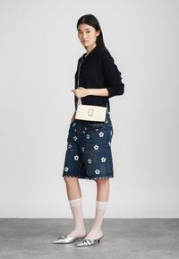 Czarny prążkowany kardigan, niebieskie dżinsowe szorty z białymi kwiatowymi haftami, srebrne mule, przezroczyste białe skarpetki oraz kremowa torebka na ramię.