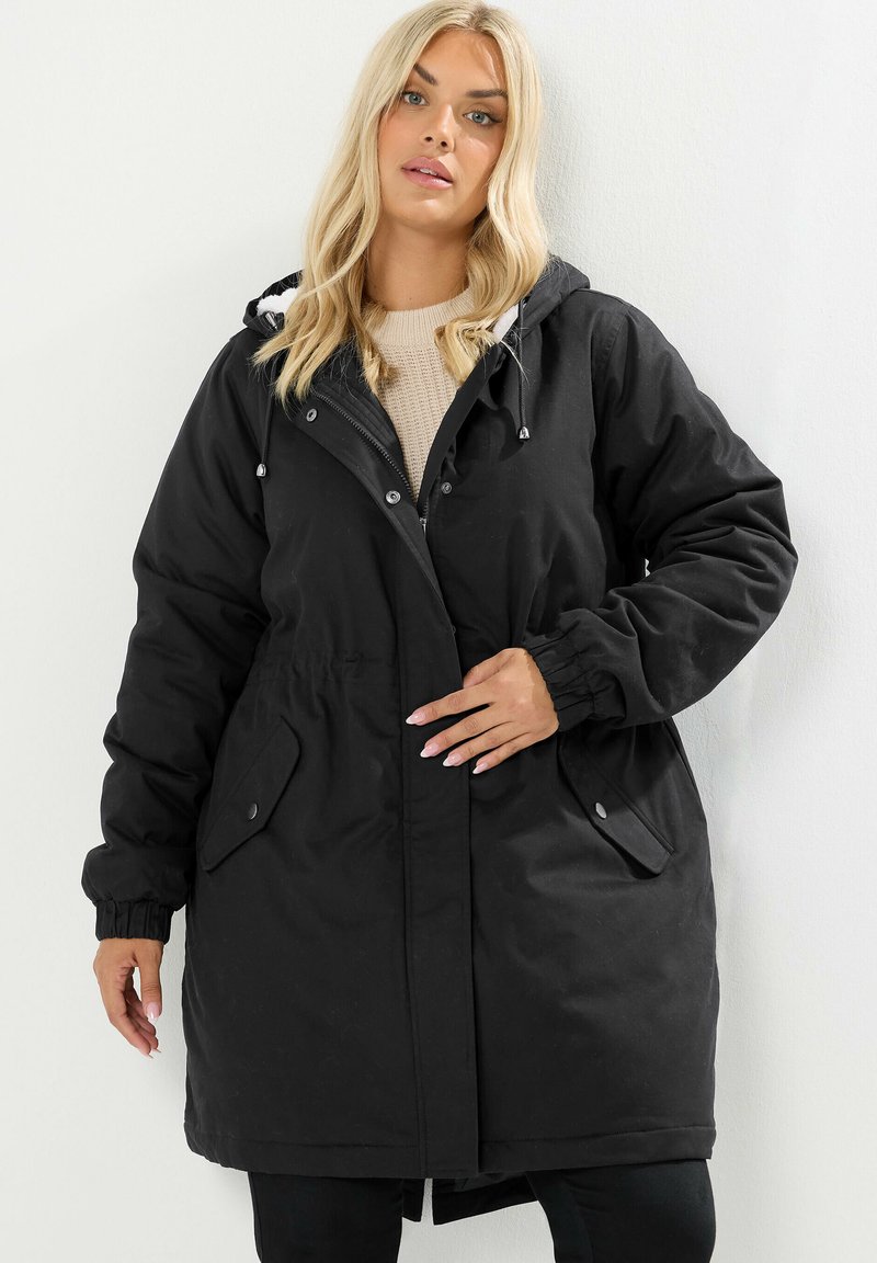 Svart huva parka med blixtlås och tryckknappar, elastiska mudd, dragsko i midjan och sidfickor. Slät textur, midilång design.