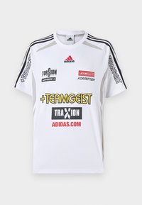 Bílý sportovní dres s krátkým rukávem, s černými pruhy na ramenech. Více log v červené a žluté barvě; texturovaná látka s hladkým povrchem.