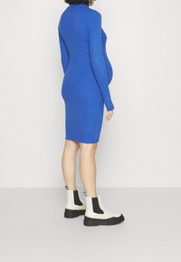 Blå stickad klänning med långa ärmar och hög halsringning, bärs med krämfärgade och svarta ankelstövlar med tjock sula.