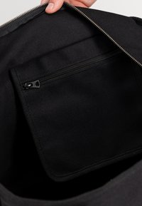 Czarna torba materiałowa wewnątrz z kieszonką na zamek błyskawiczny. Teksturowana podszewka i srebrny zamek dopełniają minimalistyczny design.