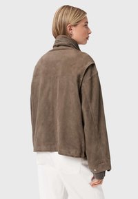 Bruine suède jas met een hoge kraag, een relaxte pasvorm en verlaagde schouders. Voorzien van drukknoopsluiting op de mouwen en een gestructureerde stof.