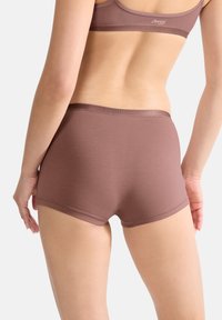 Ruskeat puuvillasekoiteshortsit pojille, joissa on sileä vyötärönauha. Shortsien muoto on saumaton ja materiaali pehmeä, kuva otettu takaapäin.