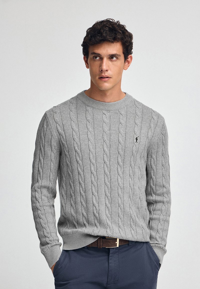 Suéter gris de punto trenzado con cuello redondo y puños acanalados. Presenta un intrincado patrón retorcido. Pequeño logo en el pecho.