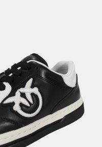 Sneaker in pelle bianca e nera con punta arrotondata, chiusura con lacci e logo ricamato sul lato, dotata di suola in gomma testurizzata.