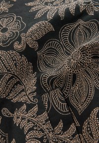 Tissu noir avec des motifs floraux et feuillus beiges complexes, brodés en fines lignes créant un design texturé.