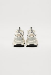 Baskets blanches et grises avec une semelle épaisse, une tige en mesh et en synthétique, des languettes de tirage et une marque bien visible sur les talons. Semelle extérieure noire plate.