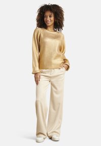 Gold ribbed sweater with long sleeves, paired with wide-leg cream trousers and white sneakers; smooth texture and relaxed fit.