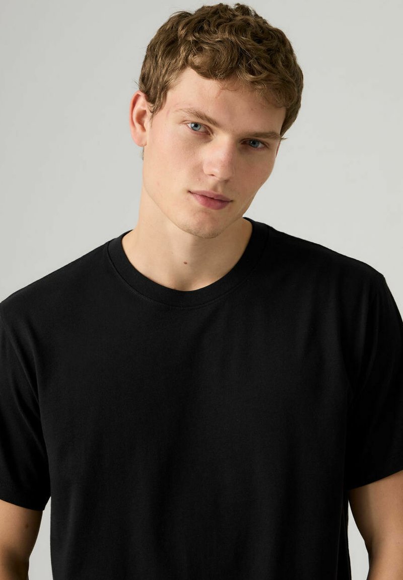 T-shirt nera in cotone con maniche corte e scollatura rotonda, caratterizzata da una texture liscia e un design semplice e classico.