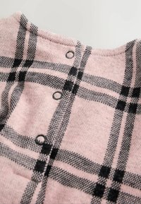 Lyserød og sort ternet sweater med rund halsudskæring, med sorte knapper langs ryggen og et struktureret strikmønster.