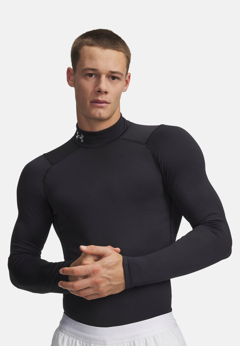 Giovane uomo con capelli corti che indossa una maglia nera a compressione a maniche lunghe e pantaloncini sportivi bianchi, con le mani giunte davanti.