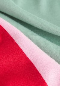 Knit fabric in red, light pink, and green. Features a soft texture with a blend of colors, showcasing a layered striped design.