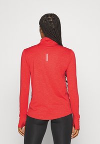 Rode sportieve top met lange mouwen en een hoge kraag, voorzien van een subtiele lijn aan de achterkant en een gebogen zoom, gemaakt van een zachte stof.