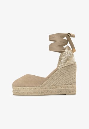 Alpargata cuña de lona beige con suela de cuerda trenzada y cordones para atar al tobillo, con detalle tejido en el contrafuerte del talón.