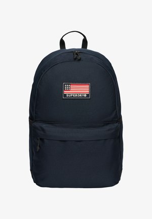 Mochila azul marino con bolsillo frontal con cremallera, asa superior y parche del logo de Superdry que presenta una bandera americana estilizada.