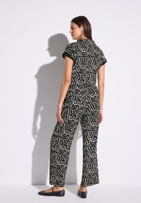 Mono de estampado en blanco y negro con mangas cortas, cintura alta y diseño de pierna ancha. Textura suave y sutil brillo.