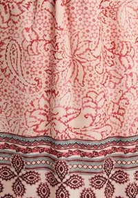 Tessuto di cotone con intricati motivi floreali e geometrici in tonalità di rosso e rosa, con un bordo decorativo in tonalità più scure.