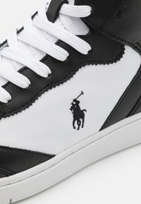 Svart och vit sneaker i läder, med vita snörningar och en broderad logotyp. Texturerad sula och slät ovandel.