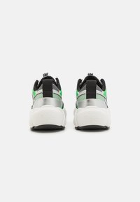 Schwarze und grüne Sneakers mit strukturiertem Mesh und glänzenden silbernen Akzenten, ausgestattet mit einer gepolsterten weißen Sohle und einem gepolsterten Fersenbereich für zusätzlichen Komfort.