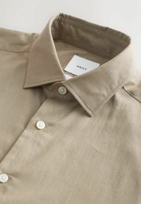 Chemise en lin beige à boutons, col pointu et boutons blancs, étiquette de marque "NEXT" visible à l'intérieur du col.
