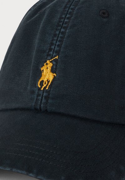Sötét tengerészkék baseballsapka sárga hímzett logóval, amely egy póni lovagló pólójátékost ábrázol ütővel a kezében.