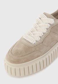 Baskets en suede beige avec semelle en caoutchouc crème épaisse et lacets crème tressés ; texture lisse avec des détails surpiqués sur le dessus.