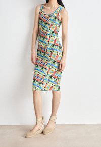 Bunt gemustertes, tailliertes Kleid mit lebendigem abstraktem Muster, aus dehnbarem Material, knielang, kombiniert mit beigen Espadrilles.
