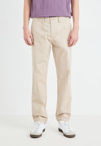 Beige cotton pants with a straight leg design, featuring a button closure and side pockets, paired with white sneakers.