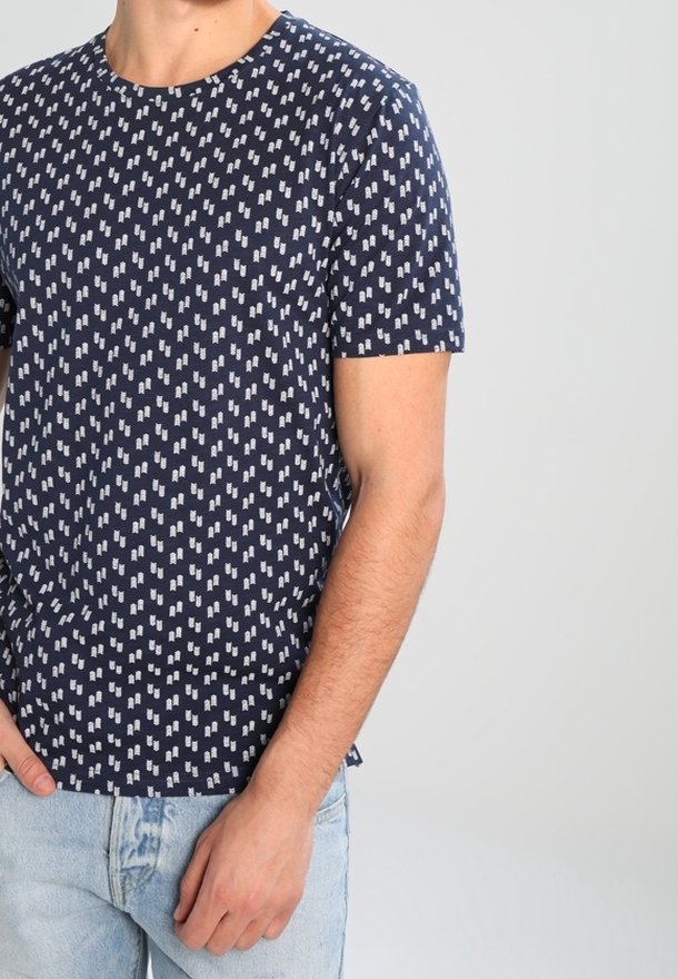 Camiseta de manga corta azul marino con un patrón geométrico blanco repetido; fabricada en algodón, cuenta con un cuello redondo y un corte relajado.