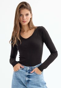 Top negro de manga larga con diseño de cuello en V, hecho de una tela suave. Combinado con unos vaqueros de mezclilla azul claro de cintura alta, que presentan bolsillos delanteros.