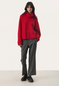 Rode gebreide oversized coltrui met ribbelstructuur, gecombineerd met een grijze wijde pantalon en zwarte chunky laarzen.