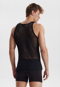 Sort mesh tank top med en rund kant, der har et stramt strikket mønster, brede ærmegab og en glat kant langs halsudskæringen og skuldrene.