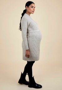 Hellgraues, gestricktes Umstandskleid mit Zopfmuster und bequemer Passform, kombiniert mit schwarzen Stiefeletten und blickdichten schwarzen Leggings.