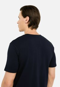 Maglietta di cotone blu navy con maniche corte, collo rotondo e una superficie liscia, che mostra la vista posteriore e dettagli di cucitura minimal.