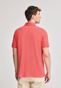 Polo de manga corta en color coral, fabricado en una tela suave con cuello clásico y aberturas laterales en el dobladillo para facilitar el movimiento.