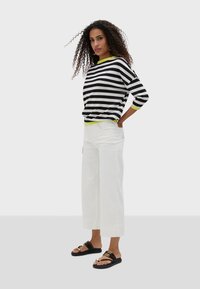 Black and white striped top with green trim, white wide-leg pants, and black slide sandals with gold accents. Casual, relaxed fit.