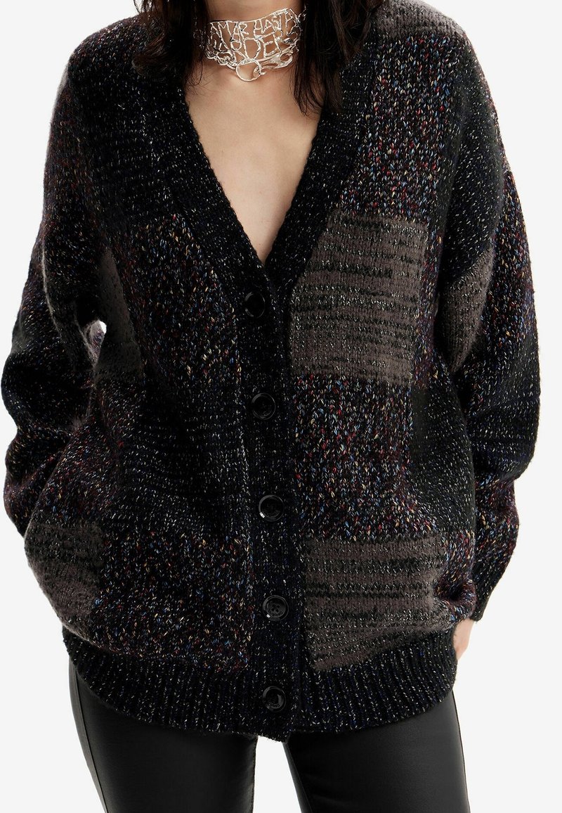 Cardigan tricoté dans des tons foncés avec un design patchwork. Il présente un col en V, une patte de boutonnage à l'avant et un tissu texturé avec des touches de couleur.