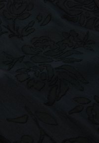 Zwarte stof met een geprofileerd bloemmotief, voorzien van verhoogde omtrekken van rozen en bladeren, wat een subtiele, gelaagde uitstraling creëert.