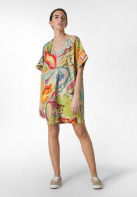 Abito corto multicolore con scollatura a V, maniche oversized e audaci motivi astratti in verde, rosso e blu su un tessuto leggero.