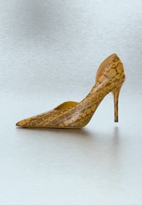 Chaussure à talon haut à bout pointu avec motif en cuir de serpent jaune et marron sur une surface lisse et claire.
