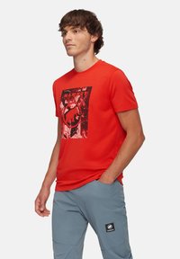 Röd bomull t-shirt med en kontrasterande svart grafisk design av en mammut och logotyp i en rektangulär ram på framsidan.
