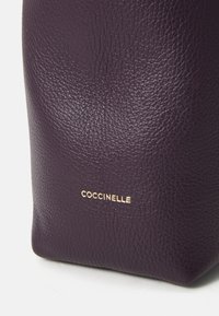 Purple textured leather bag featuring a gold logo detail. The design is structured with a flat base and rounded edges.