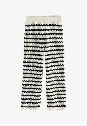 Fødder iført beige ruskindsspænde sko og sort-hvide stribede strikkede bukser, vist mod en neutral baggrund.