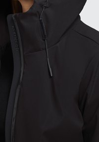 Sort vindjakke med høj krave, slankt design, justerbare snore og diskret logo-detalje langs lynlåsen.