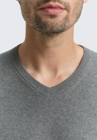 Grijze V-hals trui gemaakt van een zachte gebreide stof, met ribbels aan de randen en een gladde textuur, die nauw aansluit rond de nek en het sleutelbeen.