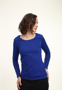 Camisa de manga larga, ajustada, de cuello redondo en vibrante tela de algodón azul. Textura suave con costuras mínimas. Llevada con pantalones negros oscuros.